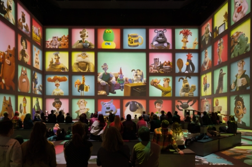 Families seated beneath a grid of Aardman characters filling Lightroom’s walls in the Aardman immersive experience