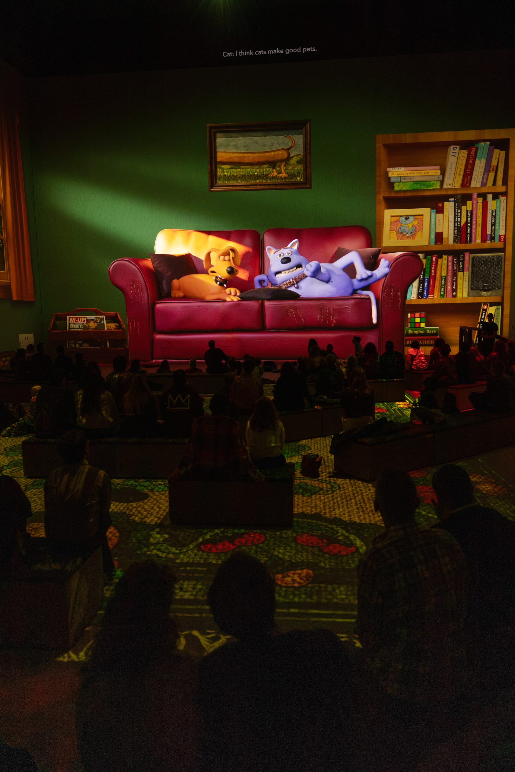 Creature Comforts characters lounge on a giant red sofa projected above audiences at Lightroom