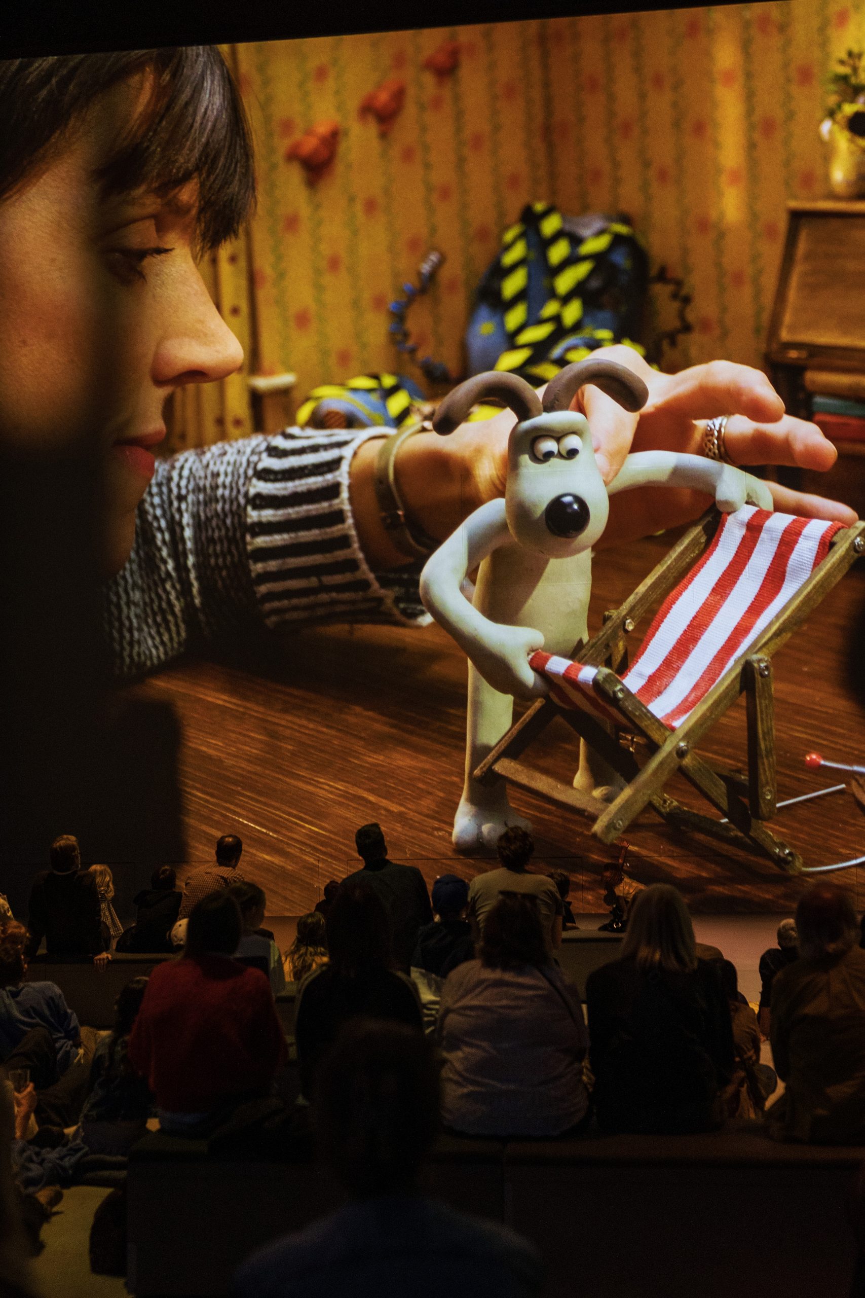A projected animator’s hand poses Gromit beside a striped deckchair, towering over the audience in the Aardman immersive experience