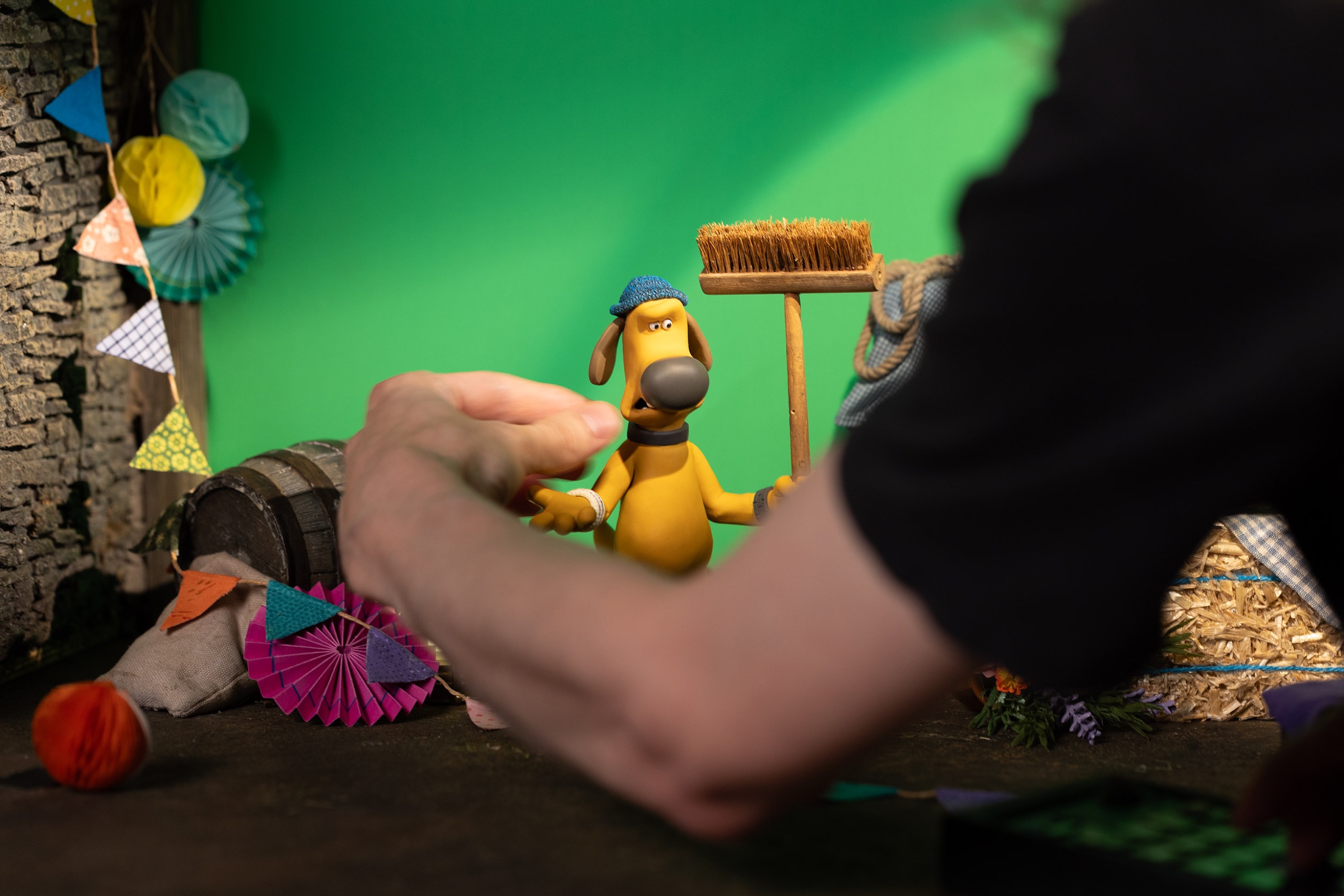 An Aardman animator poses Bitzer from Shaun the Sheep on a miniature set in front of a green screen