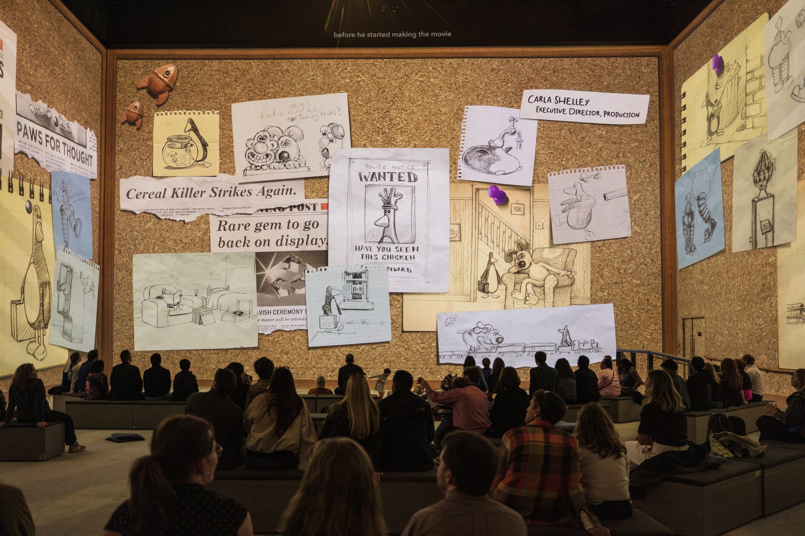 Audiences in front of a giant pinboard of Wallace & Gromit sketches and development drawings at Lightroom