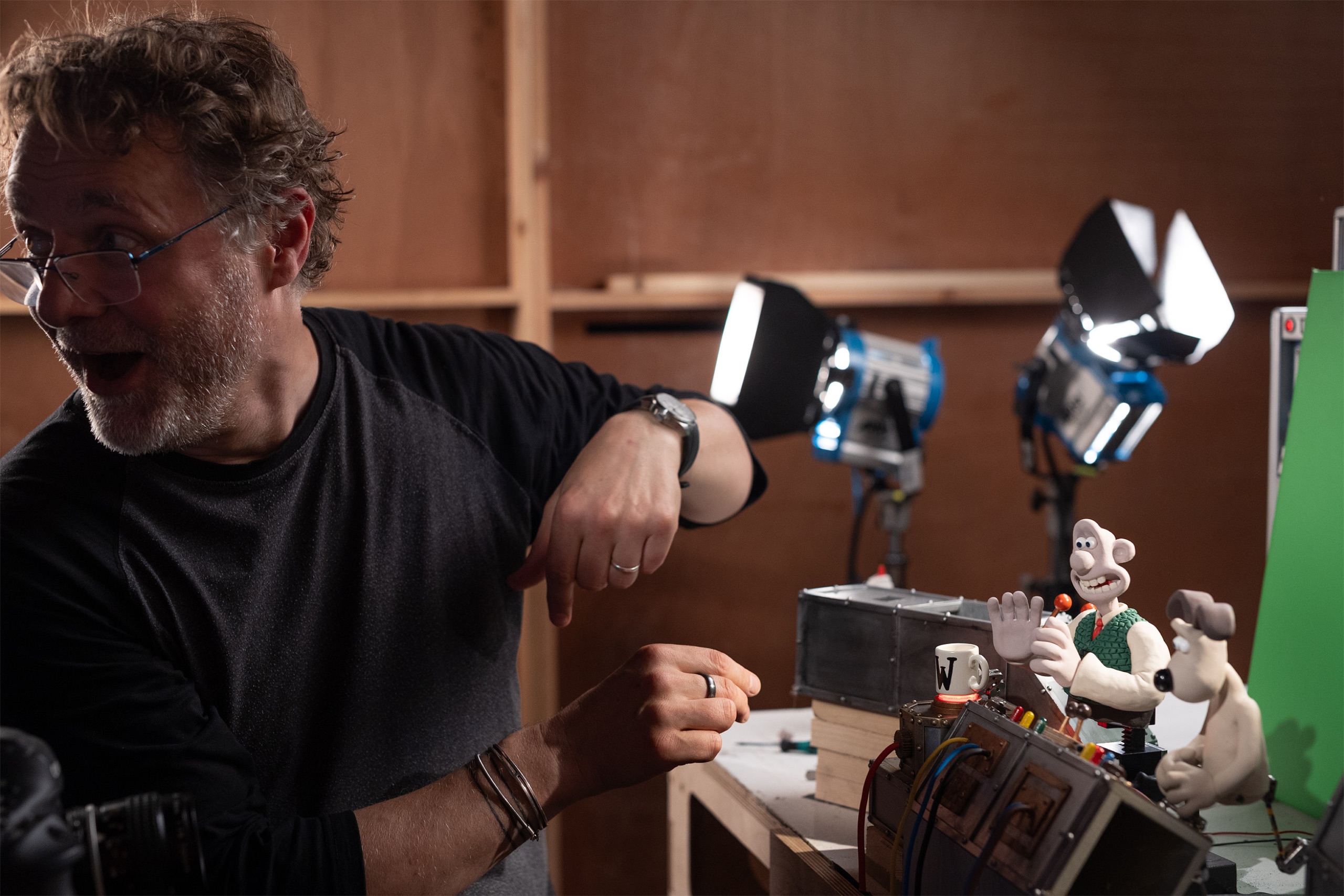 An Aardman animator beside Wallace & Gromit puppets on a lit stop-motion set