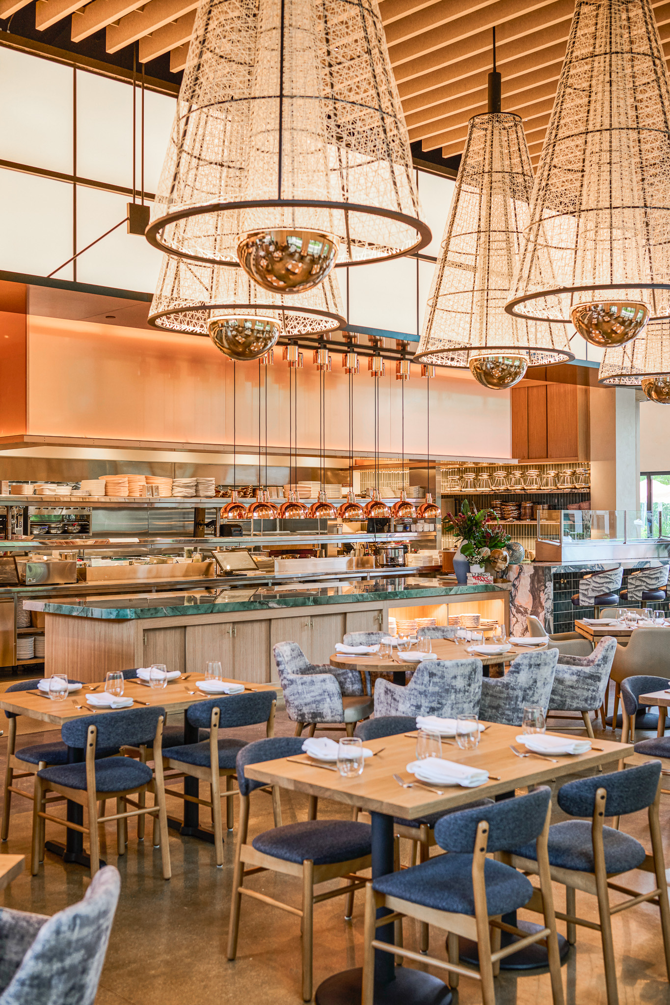 Dining tables in front of the expo kitchen and raw bar, under conical pendants