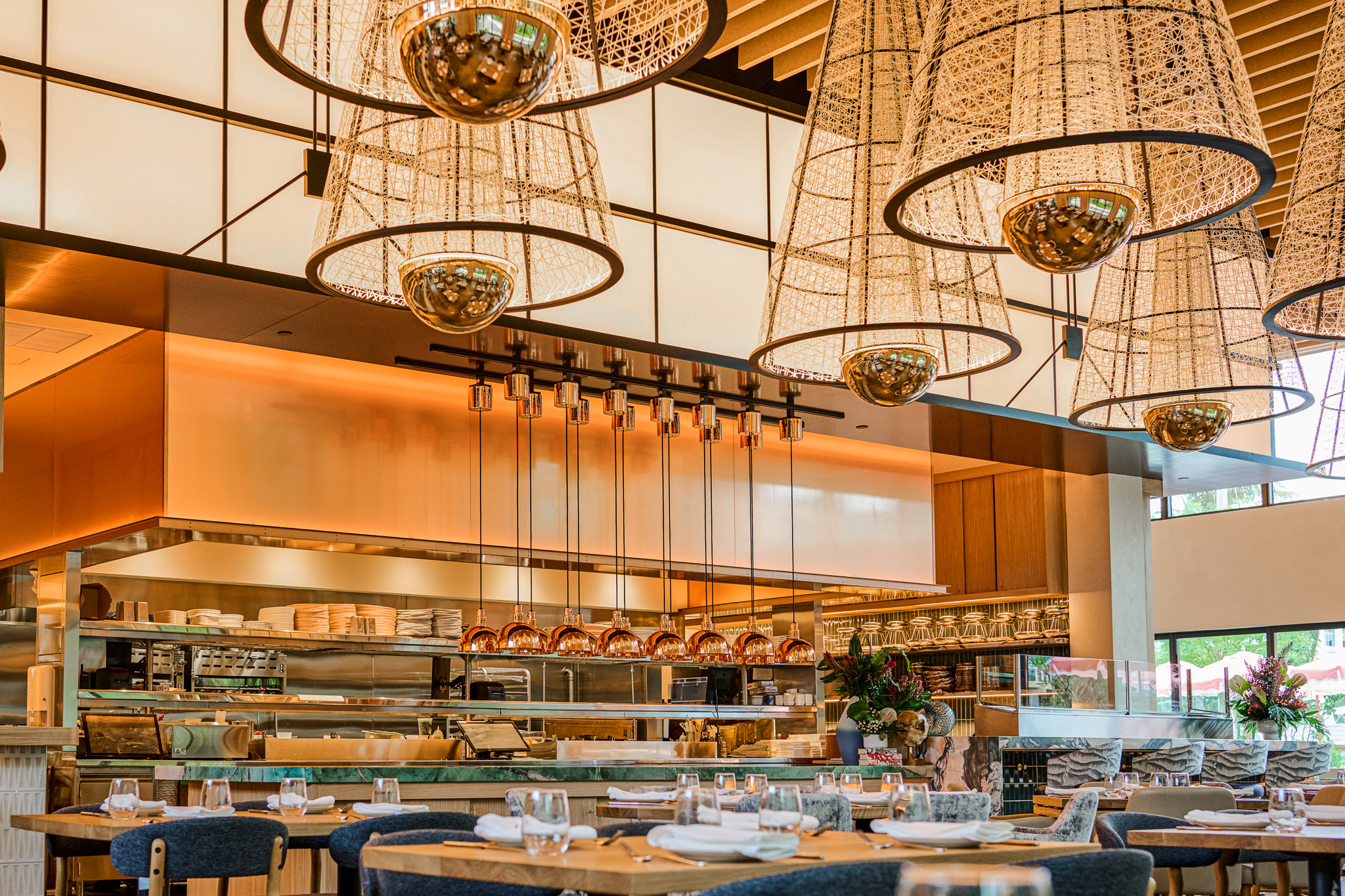 The gantry spanning the bar and expo kitchen, hung with copper pendants and framed by conical fixtures