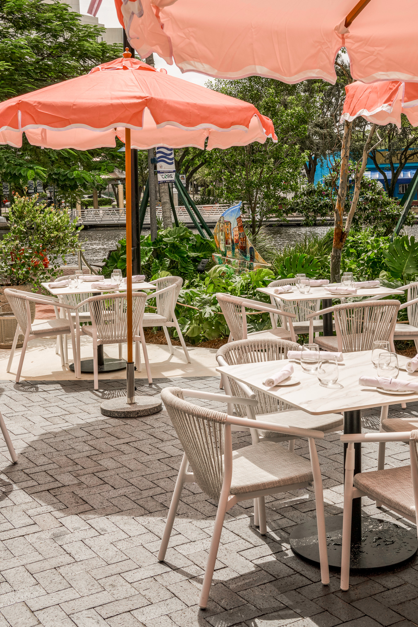 Riverside terrace tables at the restaurant under pink scalloped umbrellas, surrounded by lush planting